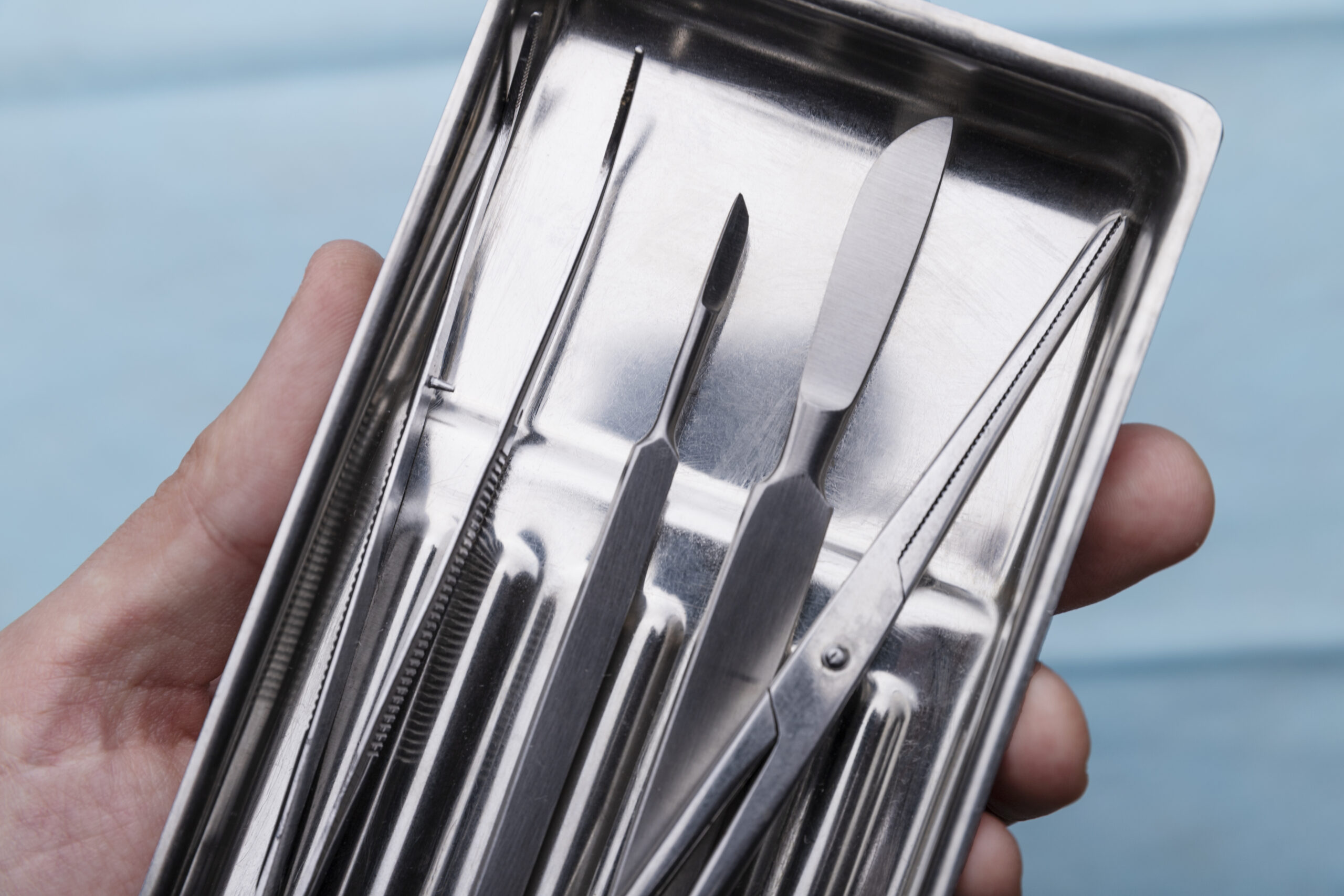 Close Up Hand Holding Tray With Medical Scalpel Tools Scaled
